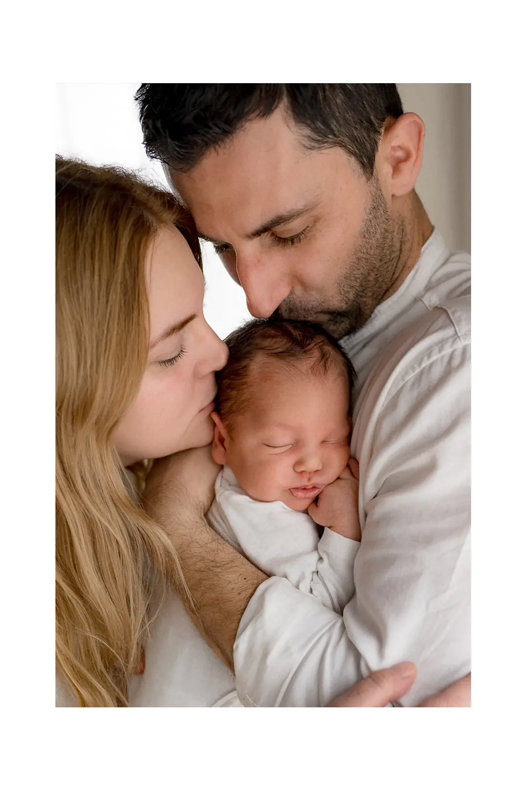 Tata i mama grle i ljube novorođenu bebu