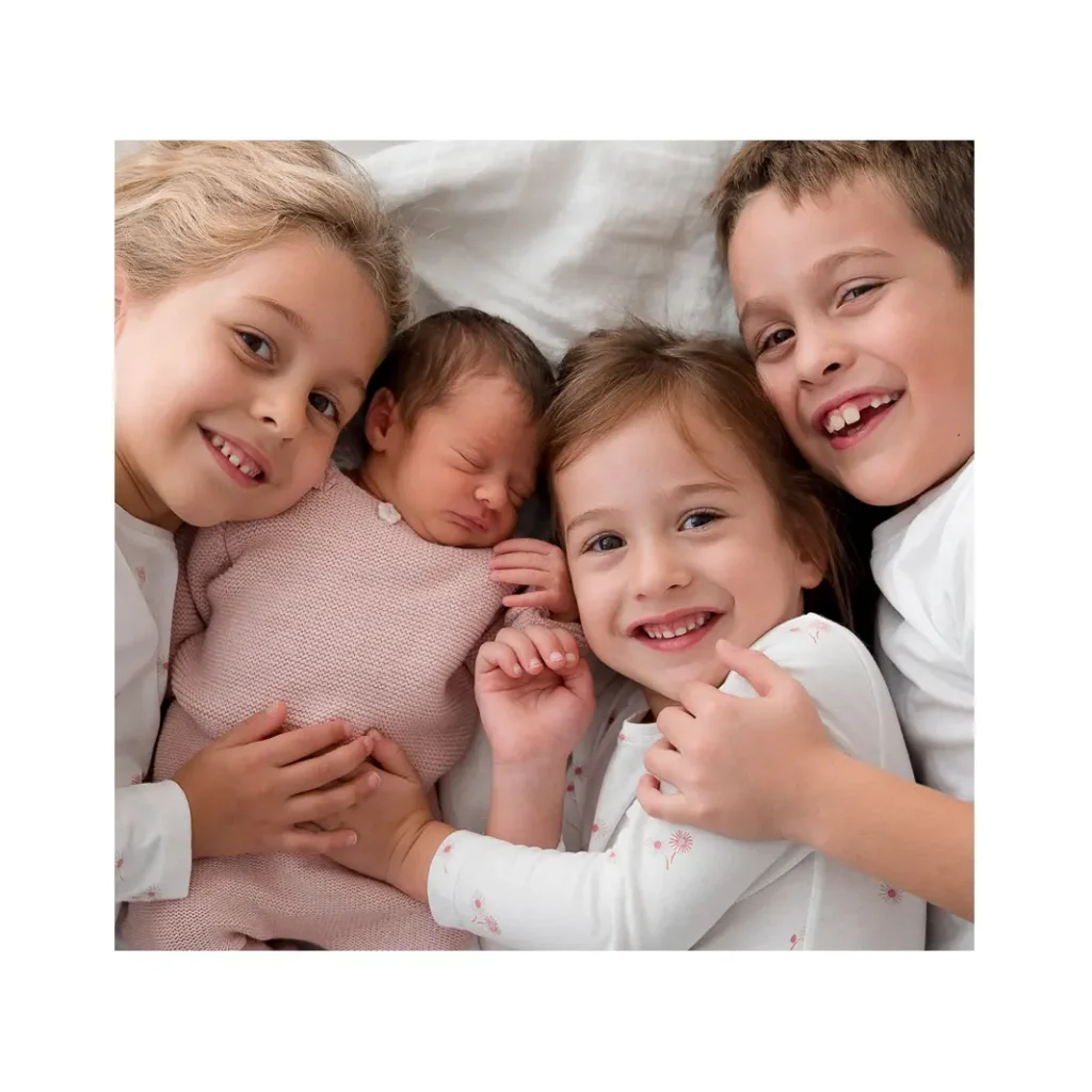 Brat i dvije seke grle novorođenu bebu na krevetu