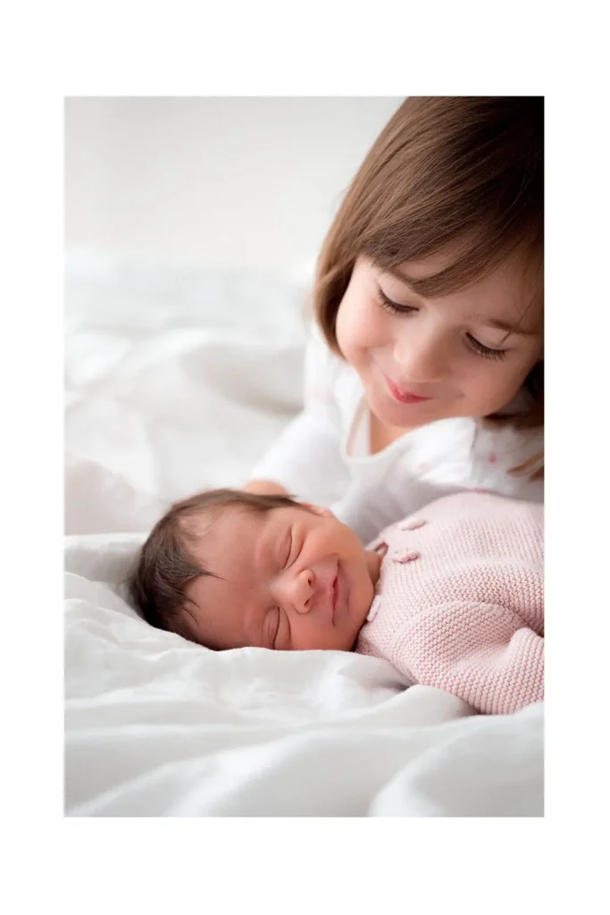Starija seka gleda novu bebu kako se smije na krevetu